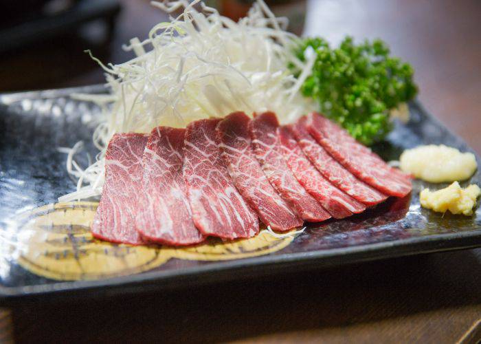 Thin slices of horse meat lined up against a bed of shredded cabbage.